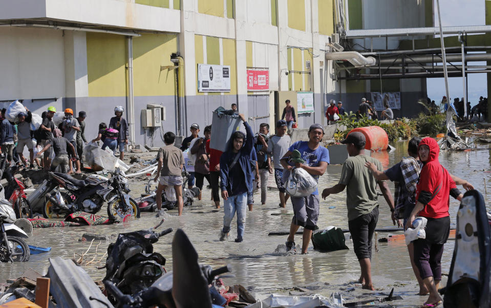 People carry items from the shopping mall which was damaged following earthquakes and tsunami in Palu, Central Sulawesi, Indonesia, Sunday, Sept. 30, 2018. Rescuers try to reach trapped victims in collapsed buildings after hundreds of people are confirmed dead in a tsunami that hit two central Indonesian cities, sweeping away buildings with massive waves. (AP Photo/Tatan Syuflana)