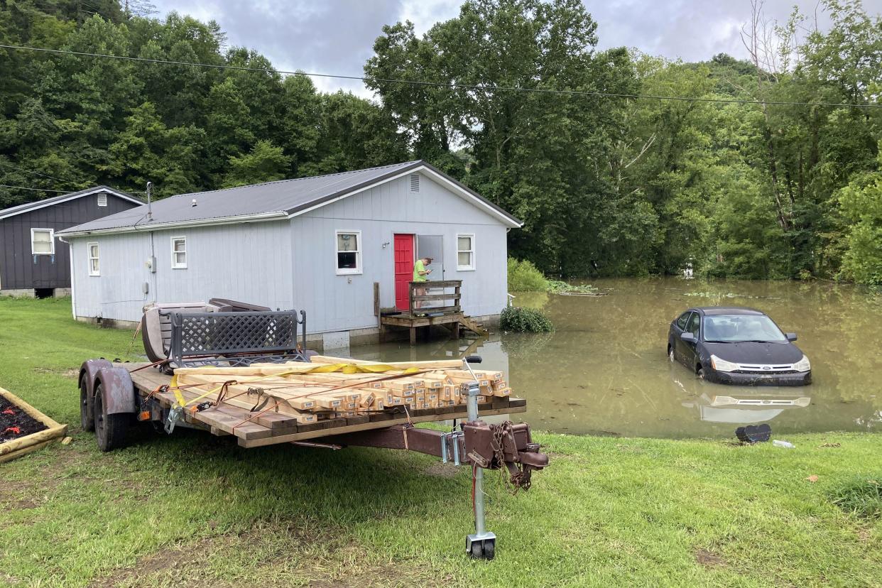 A woman glances at her phone after carrying supplies into her home in Jackson, Ky. on Friday, July 29, 2022. Flooding in the area surrounded many homes, forcing people to walk through water to get inside.