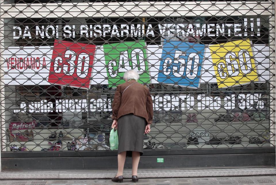A woman looks through a shuttered shop window reading: "here you can really save your money" during May Day in Rome, Tuesday, May 1, 2012. Italian Premier Mario Monti has promised to get Italy's economy growing again, but so far his government has been widely criticized by industrialists and union leaders for failing to revive growth. (AP Photo/Gregorio Borgia)