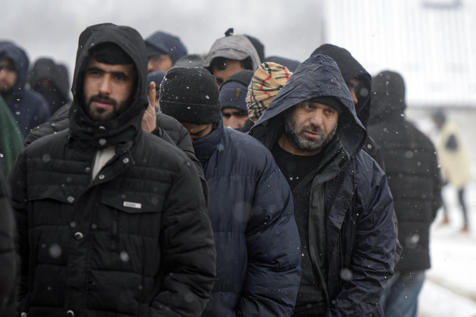 Migrants wait in lines for food handouts during a snowfall at the Lipa camp, outside Bihac, Bosnia, Friday, Jan. 8, 2021. A fresh spate of snowy and very cold winter weather on has brought more misery for hundreds of migrants who have been stuck for days in a burnt out camp in northwest Bosnia waiting for heating and other facilities. (AP Photo/Kemal Softic)