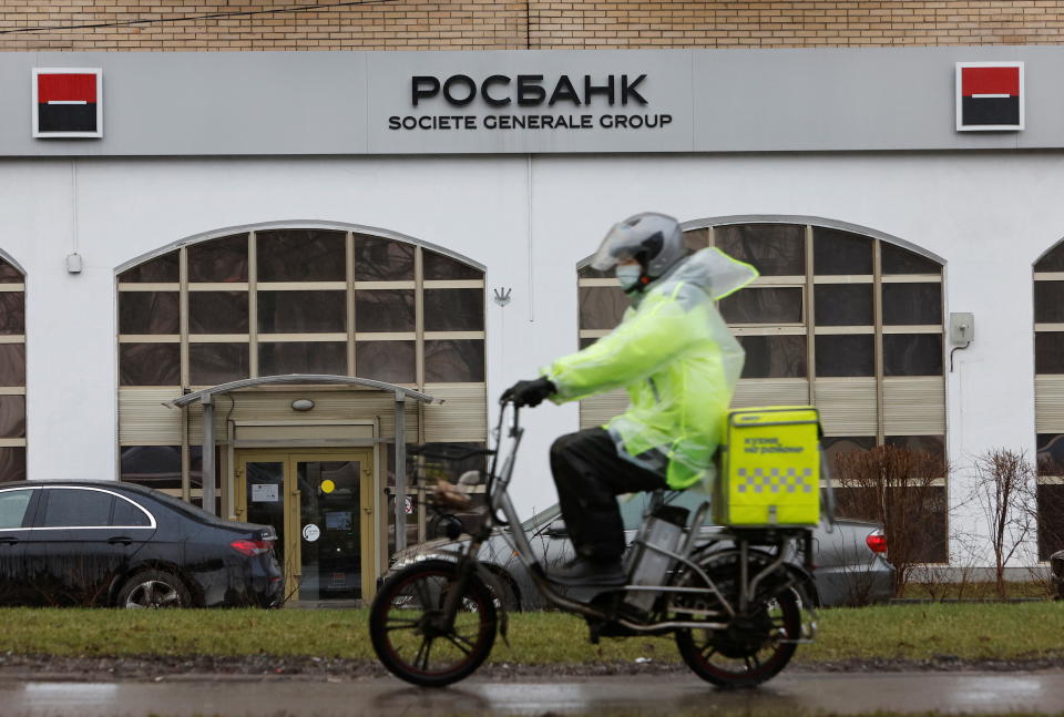 A food delivery courier on a motorcycle rides past a Rosbank branch, carrying the logo of the French bank Société Générale.