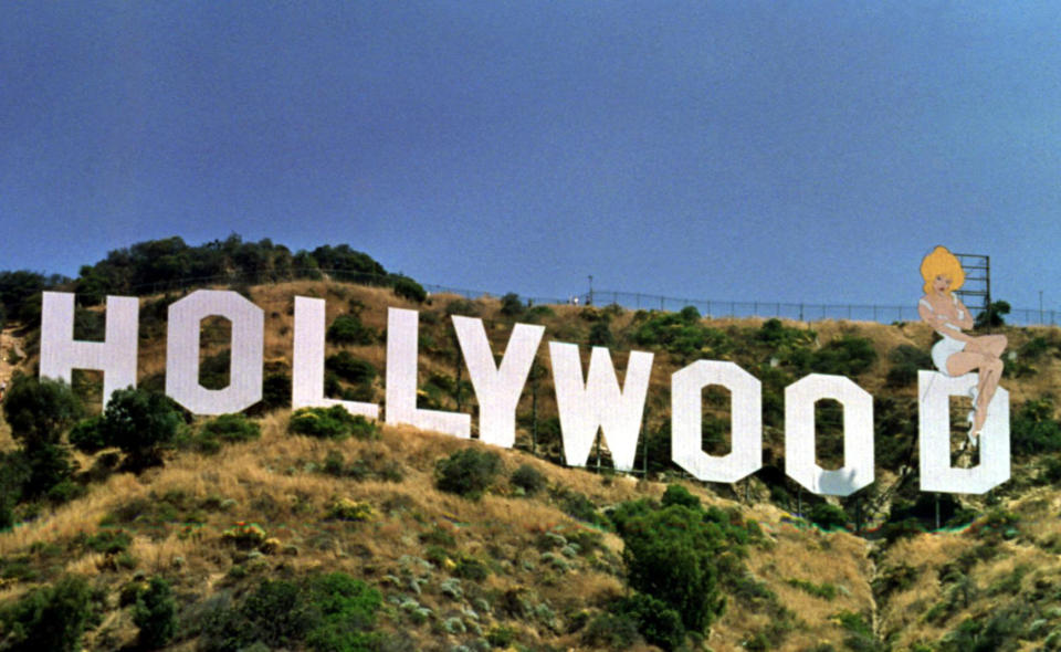 The Hollywood sign on a hillside, modified with a cartoon of Marilyn Monroe sitting on the last letter 'D'