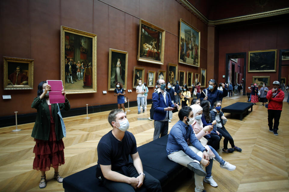 Visitors watch oil on canvas of 1807 entitled Le Sacre de Napoleon by Jacques Louis David, at the Louvre Museum, in Paris, Monday, July 6, 2020. The home of the world's most famous portrait, the Louvre Museum in Paris, reopened Monday after a four-month coronavirus lockdown. (AP Photo/ Thibault Camus)