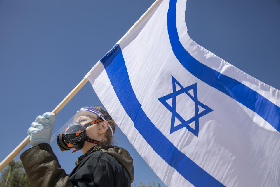 A protestor wearing a mask and gloves amid concerns over the country's coronavirus outbreak holds a flag during a protest by supporters of Prime Minister Benjamin Netanyahu in front of Israel's Supreme Court in Jerusalem, Thursday, April 30, 2020. Dozens of protesters rallied outside Israel's Supreme Court on Thursday against petitions to disqualify Benjamin Netanyahu from serving as prime minister while facing criminal indictments. (AP Photo/Ariel Schalit)