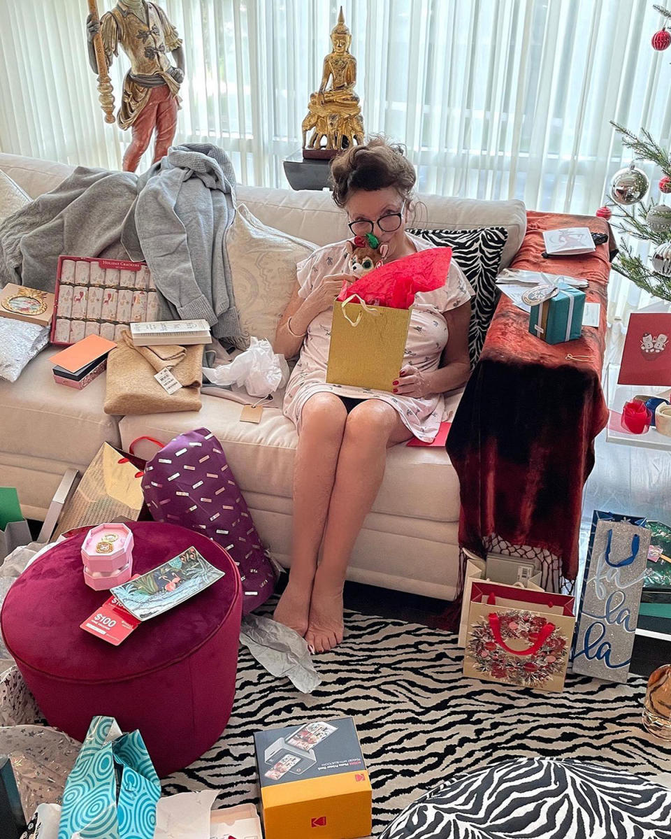 Joan Collins opening some Christmas presents on a couch