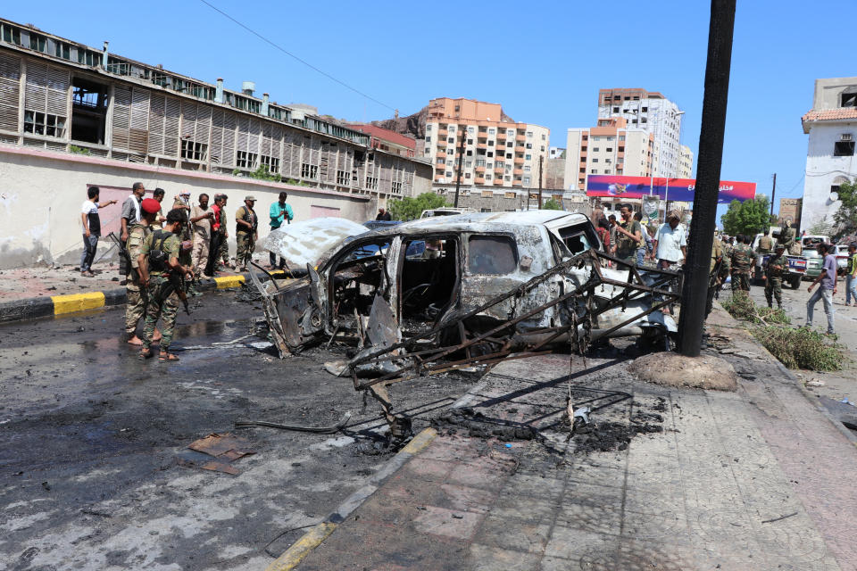 Security personnel stand amid the wreckage of a damaged vehicle at the site of a deadly car bomb attack that targeted two senior government officials, who survived, security officials said, in the port city of Aden, Yemen, Sunday, Oct. 10, 2021. Aden has been the seat of the internationally recognized government of President Abed Rabbo Mansour Hadi since the Iranian-backed Houthi rebels took over the capital, Sanaa, triggering Yemen’s civil war. (AP Photo/Wael Qubady)