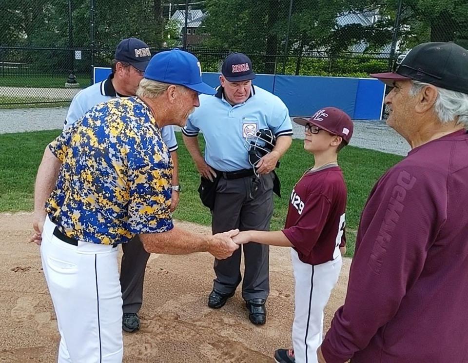 Framingham Post 74 manager Bunkie Smith, left, shakes hands with North County Post 129 bat boy Jake Downing at home plate prior to the start of a July 2021 American Legion baseball game at Doyle Field in Leominster. At right is North County manager Gregg Picucci.