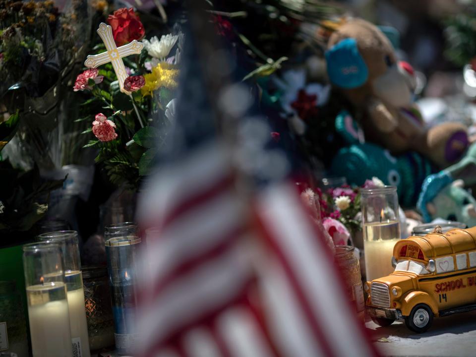 A toy yellow school bus is placed in front of a cross to honor Rojelio Torres, one of the children killed during the mass shooting in Robb Elementary School, while an American flag is seen in the foreground, Sunday, May 29, 2022, in Uvalde, Texas.