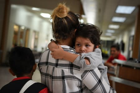 FILE PHOTO: Paola, an asylum seeker from Honduras, carries four year-old son Jesse as they wait in a ticketing line with fellow migrant families recently released from detention at a bus depot in McAllen