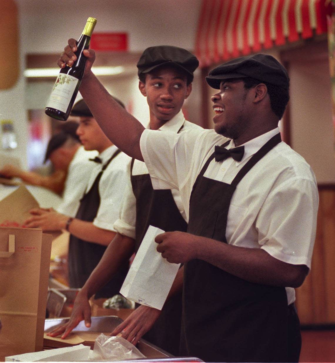 Epicure worker Billy Belony, right, teases a customer at check-out as he bags up several bottles of champagne and wine. Worker Charley Etienne is at left.. Candace Barbot/Miami Herald File / 1999