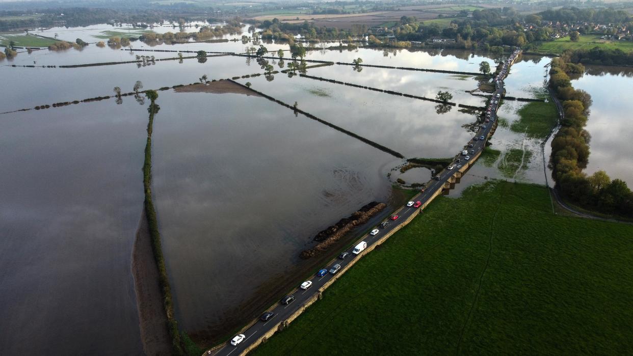 TOPSHOT - An aerial photograph taken on October 24, 2023 shows vehicles travelling along the Swarkestone Bridge, in the Village of Swarkestone, in Derbyshire, as fields are flooded following the storm Babet. A fifth death was confirmed in the United Kingdom on October 23, 2023 following the torrential rains and high winds brought by Storm Babet, which caused extensive flooding across the country. (Photo by Justin TALLIS / AFP) (Photo by JUSTIN TALLIS/AFP via Getty Images)