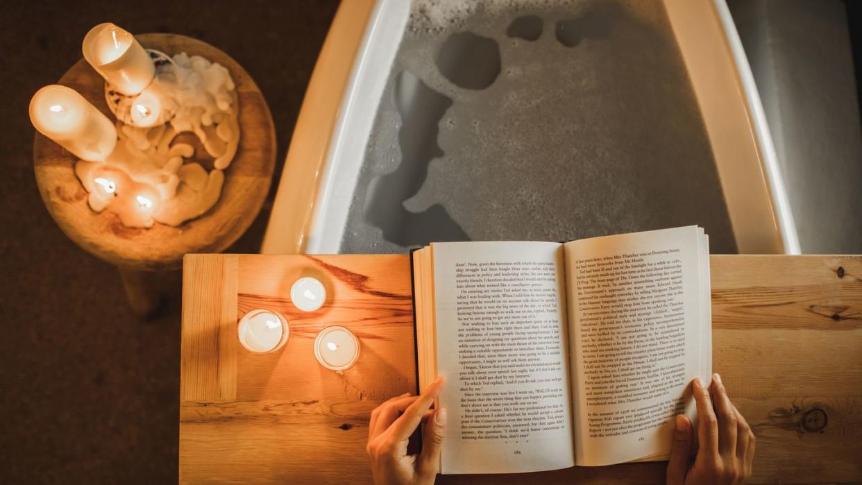 woman reading book in bath cozy and romantic evening with candles, self care and relaxation