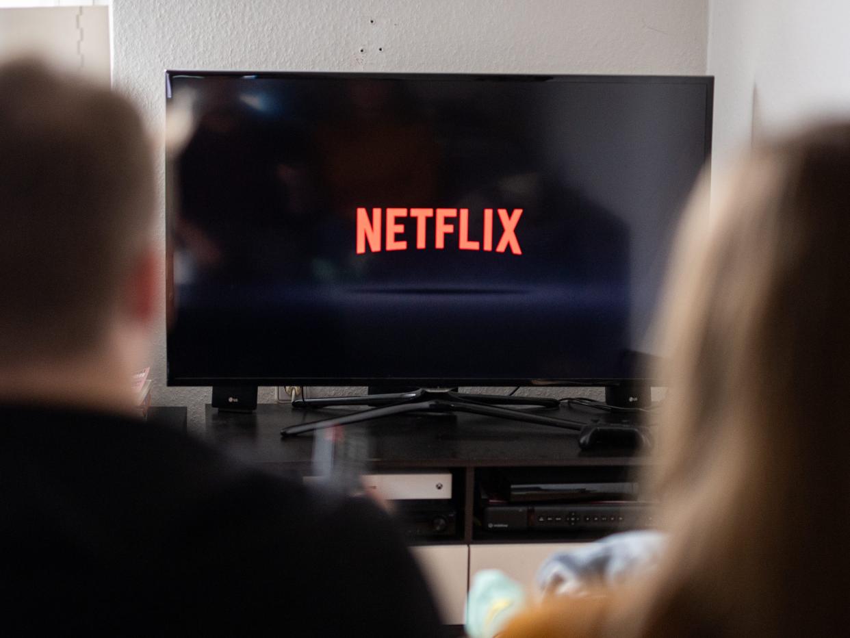 A couple sits in front of a television with the Netflix logo on it.