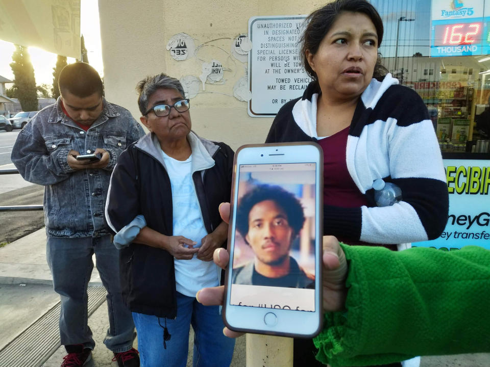FILE - In this March 10, 2019 file photo neighbors react as they look at a cellphone picture of University of Southern California student Victor McElhaney, shown by a television reporter near the scene of a crime in Los Angeles. A suspected gang member has been charged with killing the University of Southern California music student during an off-campus robbery attempt. The Los Angeles County District Attorney's Office says 23-year-old Ivan Hernandez was charged Tuesday, July 2, 2019, with one count of murder during an attempted robbery and murder while being an active participant in a criminal street gang. (AP Photo/Damian Dovarganes, File)