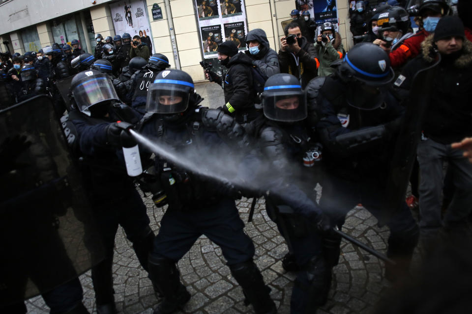 A riot police officer uses a spray gains demonstrators during a protest, Saturday, Dec.12, 2020 in Paris. Protests are planned in France against a proposed bill that could make it more difficult for witnesses to film police officers. (AP Photo/Thibault Camus)