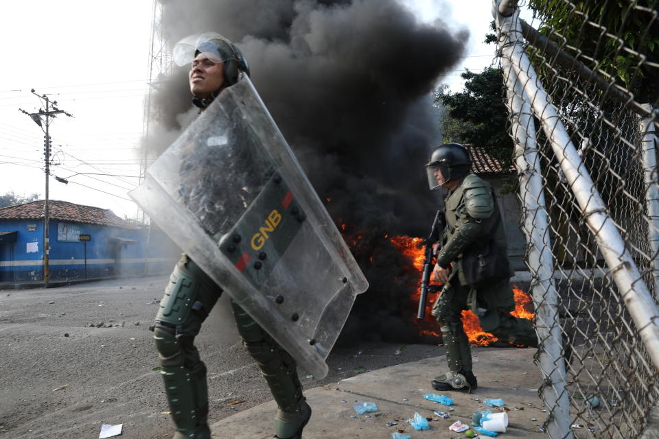FILE - In this Feb. 23, 2019 file photo, officers of the Bolivarian National Guard run during clashing with residents who cleared a barricaded border bridge attempting to bring humanitarian aid into the country, in Urena, Venezuela, near the border with Colombia. One month after opposition leader Juan Guaido declared himself Venezuela's interim president, the military has shown little sign that it plans to revolt against Maduro. (AP Photo/Rodrigo Abd, File)