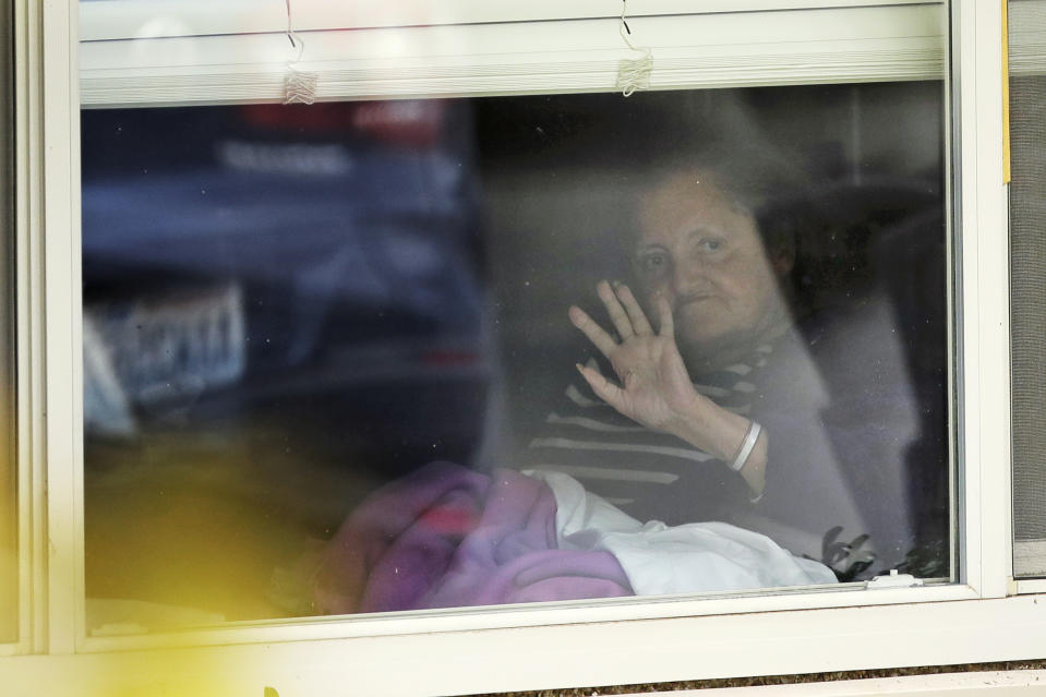 Susan Hailey, who has tested positive for the new coronavirus, waves through the window of her room at the Life Care Center in Kirkland, Wash., as her daughter leaves after a visit, Tuesday, March 17, 2020, near Seattle. In-person visits are not allowed at the nursing home, which has been at the center of the outbreak of new coronavirus in the state. (AP Photo/Ted S. Warren)