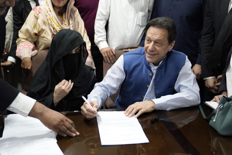 FILE - Pakistan's former Prime Minister Imran Khan, right, and Bushra Bibi, his wife, sign documents as he submits surety bond over his bails in different cases, at an office of Lahore High Court in Lahore, Pakistan, on July 17, 2023. A Pakistani court on Wednesday, Wednesday, Jan. 31, 2024 sentenced former Prime Minister Khan and his wife Bibi to 14 years in prison for corruption, prison officials said, a day after another special court convicted Khan for leaking state secrets and gave him a 10-year prison sentence. (AP Photo/K.M. Chaudary, File)