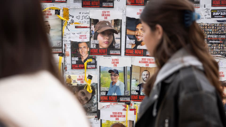 Pedestrians walk past posters of missing Israelis, including rescued hostage Louis Har (center, in blue shirt), on a wall at Hostages Square in Tel Aviv on February 12. - Oren Ziv/AFP/Getty Images