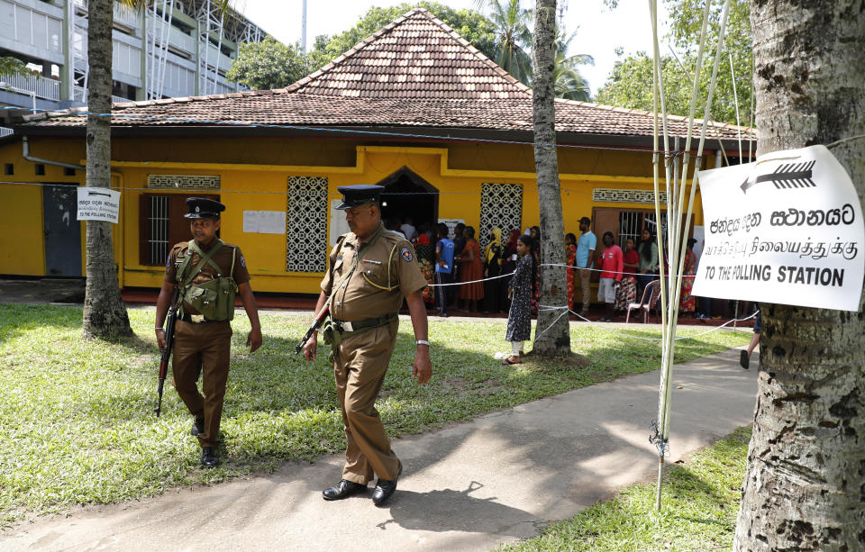 Sri Lankans queue to cast their votes as police officers patrol at a polling station during the presidential election in Colombo, Sri Lanka, Saturday, Nov. 16, 2019. Polls opened in Sri Lanka’s presidential election Saturday after weeks of campaigning that largely focused on national security and religious extremism in the backdrop of the deadly Islamic State-inspired suicide bomb attacks on Easter Sunday. (AP Photo/Eranga Jayawardena)