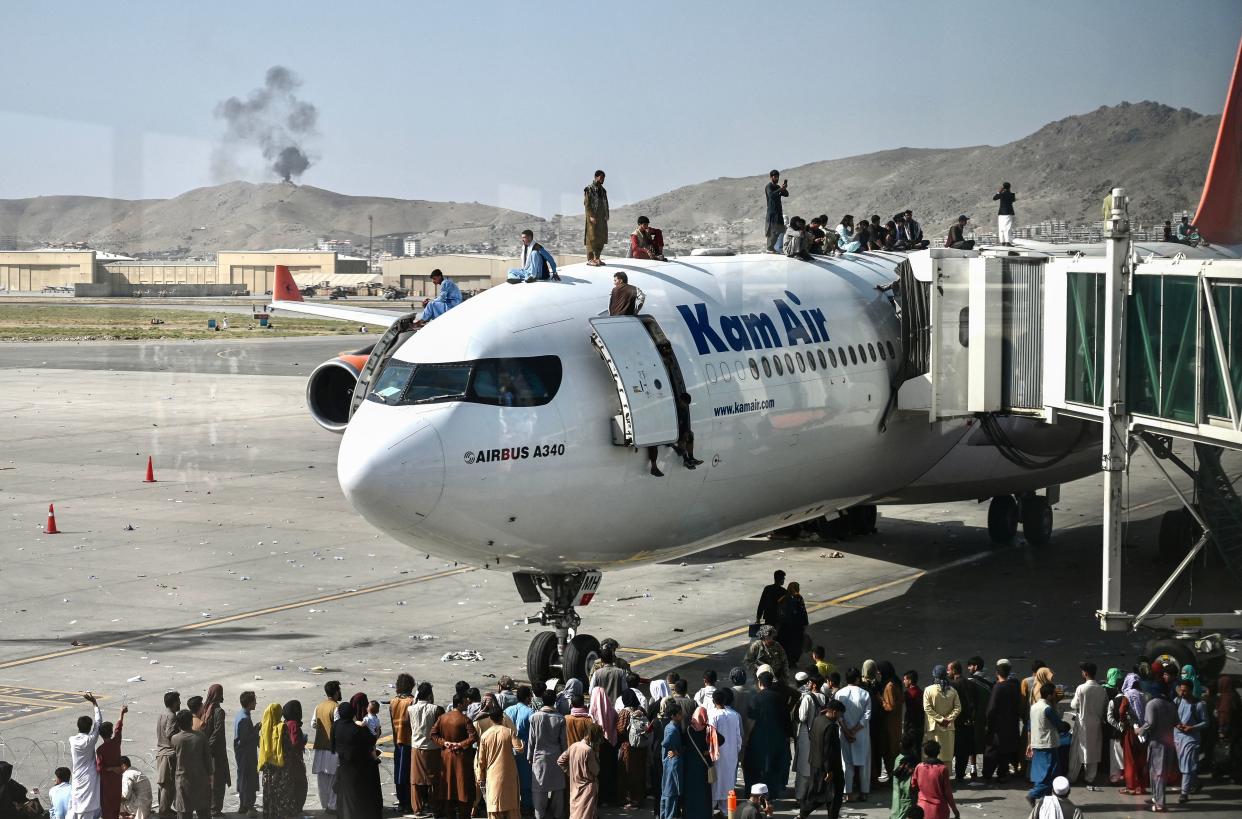 Afghan people climb atop a plane as they wait at the Kabul airport in Kabul on August 16, 2021, after a stunningly swift end to Afghanistan's 20-year war, as thousands of people mobbed the city's airport trying to flee the group's feared hardline brand of Islamist rule. (Wakil Kohsar/AFP via Getty Images)