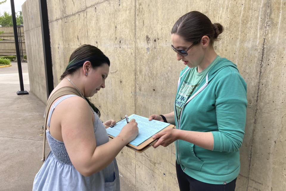 FILE - Raevahnna Richardson signs an initiative petition supporting a gun-safety ballot measure on Tuesday, June 7, 2022, outside a library in Salem, Ore., as signature gatherer Rebecca Nobiletti holds the clipboard. About half of states allow citizen initiatives. That's when groups can bypass a legislature by collecting a certain number of signatures of registered voters to put proposed laws or constitutional changes on the ballot. (AP Photo/Andrew Selsky, File)