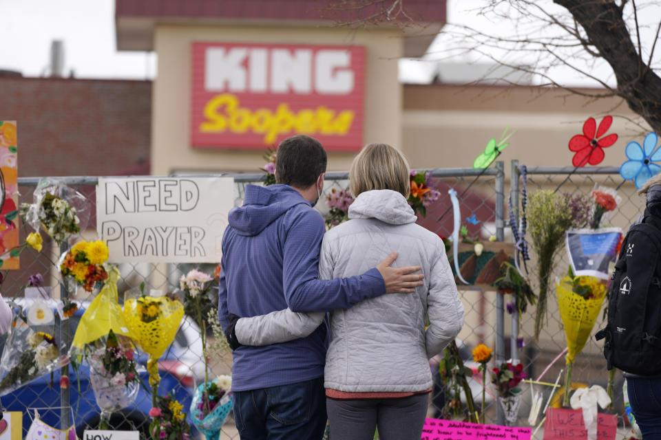 Mourners walk the temporary fence line outside the parking lot of a King Soopers grocery store, the site of a mass shooting in which 10 people died, Friday, March 26, 2021, in Boulder, Colo. (AP Photo/David Zalubowski)