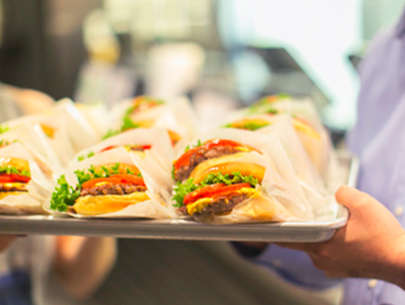 A hand holding a tray of Shake Shack burgers