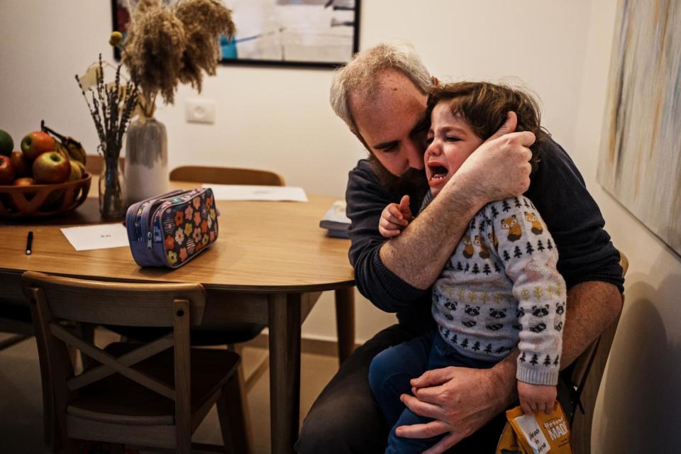 A man seated at a dining table holds a crying boy in his lap