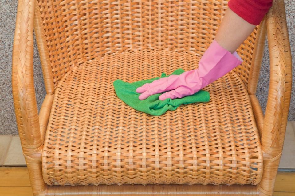 Woman wearing gloves using a microfiber towel on a wicker chair.