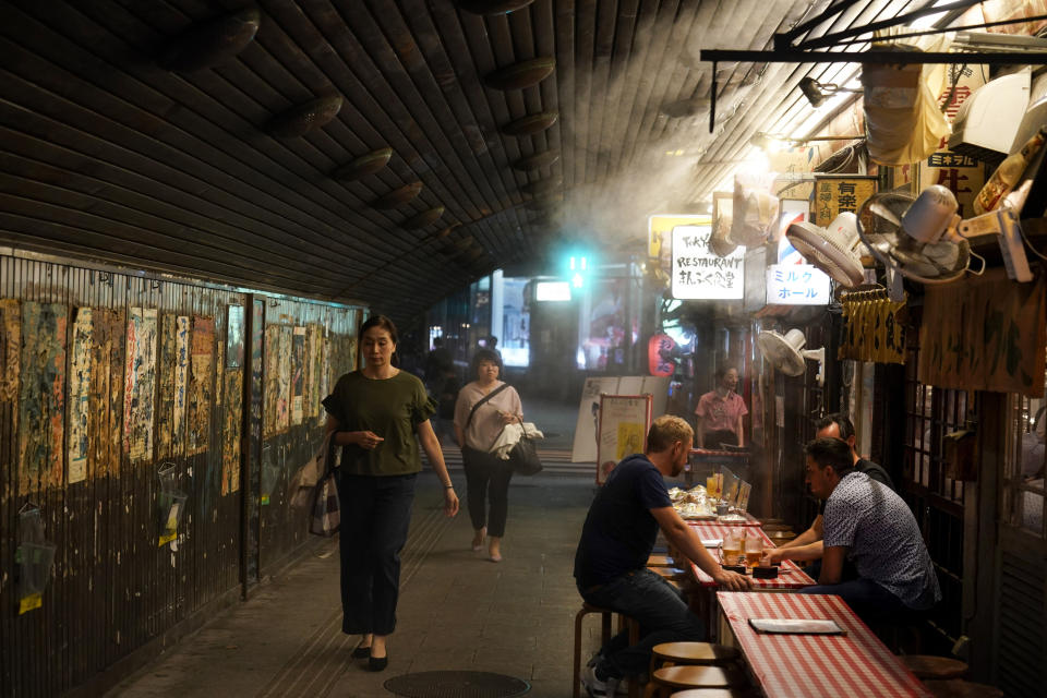 In this Monday, Aug. 19, 2019, photo, tourists dine under a mist sprayer in Tokyo. Tokyo is shaping up as a very pricey Olympics. Ticket demand is unprecedented, so scalping is sure to flourish. Hotel rates are soaring to five-six times normal. And getting here will be costly, particularly for fans from the Americas and Europe. (AP Photo/Jae C. Hong)