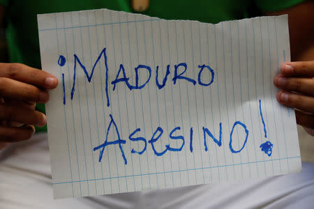 A mourner of the municipal lawmaker Fernando Alban holds a placard that reads, "Maduro murderer", during a gathering outside the headquarters of Bolivarian National Intelligence Service (SEBIN) in Caracas, Venezuela October 8, 2018. REUTERS/Carlos Garcia Rawlins