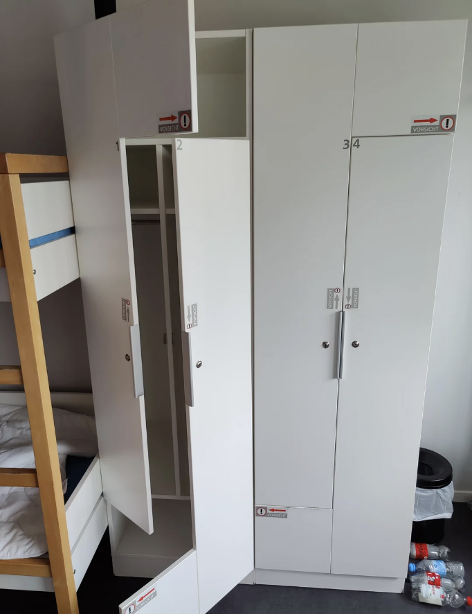 Open white lockers with numbers and some open doors are next to a bunk bed in a dorm room