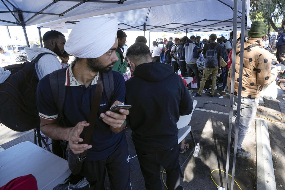 Migrants charge and use their phones in a parking lot set up to help people with travel plans, accommodation, food and shelter, Friday, Oct. 6, 2023, in San Diego. San Diego's well-oiled system of migrant shelters is being tested like never before as U.S. Customs and Border Protection releases migrants to the streets of California's second-largest city because shelters are full. (AP Photo/Gregory Bull)
