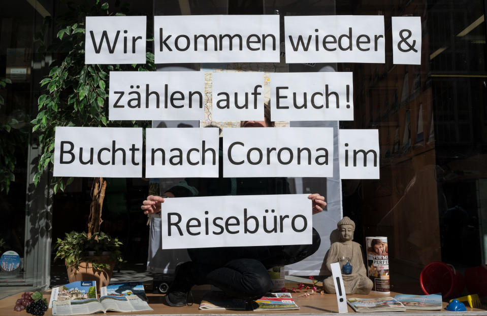 23 March 2020, North Rhine-Westphalia, Dortmund: An employee of a travel agency sticks individual sheets of paper with the inscription "We will come back & count on you! Bucht nach Corona im Reisebüro" into the shop window. Collections of more than two people are prohibited throughout Germany, shops and restaurants are closed. Photo: Bernd Thissen/dpa (Photo by Bernd Thissen/picture alliance via Getty Images)