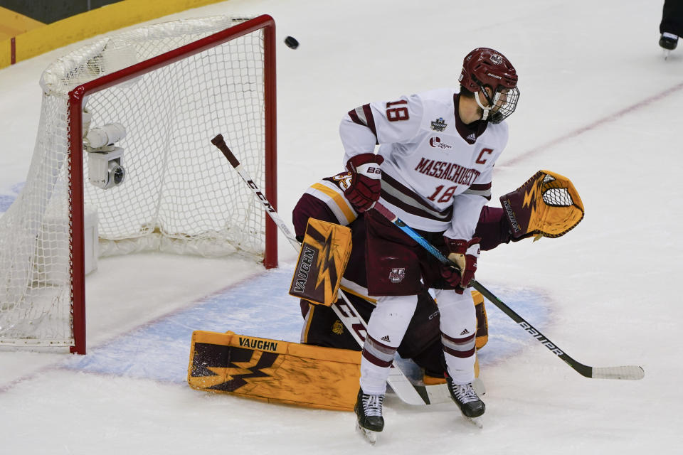 A puck shot by Massachusetts' Zac Jones whizzes past Jake Gaudet (18) and Minnesota Duluth goaltender Zach Stejskal for a goal during the first period of an NCAA men's Frozen Four hockey semifinal in Pittsburgh, Thursday, April 8, 2021. (AP Photo/Keith Srakocic)