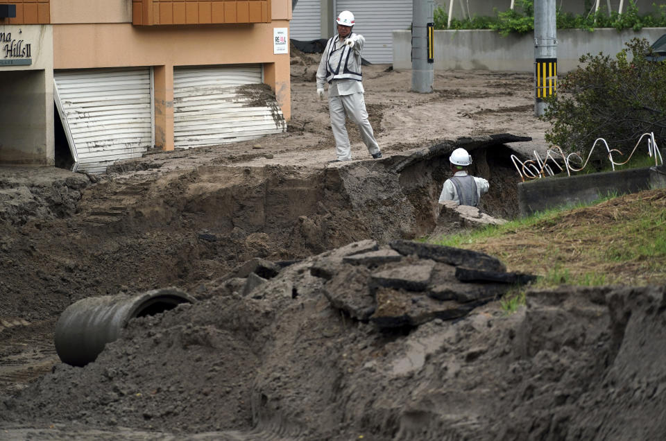 Workers speak over a street buried in mud caused by ground liquefaction after a powerful earthquake in Kiyota ward of Sapporo, Hokkaido, northern Japan, Saturday, Sept. 8, 2018. Thursday's powerful earthquake hit wide areas on Japan's northernmost main island of Hokkaido. Some parts of the city were severely damaged, with houses atilt and roads crumbled or sunken. A mudslide left several cars half buried, and the ground subsided in some areas, leaving drainpipes and manhole covers protruding by more than a meter (yard) in some places. (AP Photo/Eugene Hoshiko)