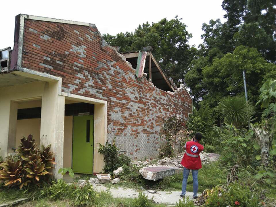 In this handout photo provided by the Philippine Red Cross, a volunteer takes photos of a damaged structure after a strong earthquake struck in Cataingan, Masbate province, central Philippines on Tuesday Aug. 18, 2020. A powerful and shallow earthquake struck a central Philippine region Tuesday, prompting people to dash out of homes and offices but there were no immediate reports of injuries or major damage. (Philippine National Red Cross via AP)