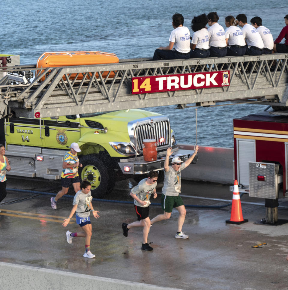 In this photo provided by the Florida Keys News Bureau, entrants in the annual Seven Mile Bridge Run are cooled by spray nozzles as they run under a City of Marathon fire truck's ladder Saturday, April 1, 2023, near Marathon, Fla. The annual event attracted 1,500 runners that traversed the longest of 42 bridges over water that help comprise the Florida Keys Overseas Highway. Joanna Stephens, 28, of Atlanta won the overall women's title and Vaclav Bursa, 15, of Big Pine Key, Fla., won the overall men's division. (Andy Newman/Florida Keys News Bureau via AP)