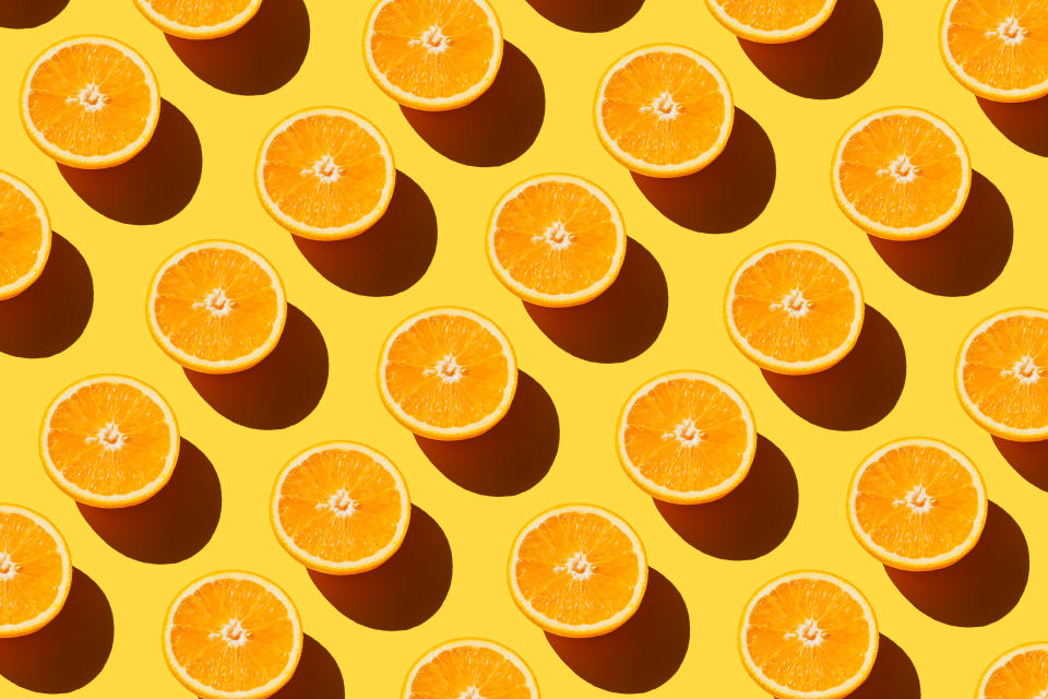 A number of cut oranges against a yellow background.