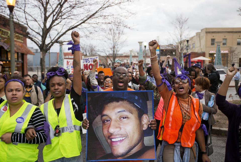 FILE - In this March 11, 2015 file photo, Brandon Marshall carries a photo of Anthony Hill as protesters march through the street demonstrating Hill's shooting death by a police officer, in Decatur, Ga. Robert Olsen, then a DeKalb County police officer, shot and killed 27-year-old Anthony Hill in March 2015. Olsen was indicted on charges including felony murder. Jury selection for his trial is scheduled to start Monday, Sept. 23, 2019. (AP Photo/David Goldman, File)