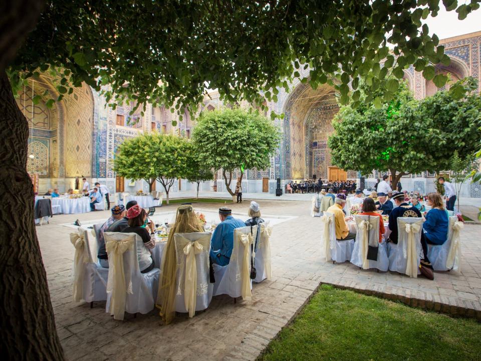 People dining outside on a courtyard surrounded by orante architecture and trees.