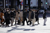 People wearing protective masks to help curb the spread of the coronavirus walk along a pedestrian crossing Friday, Jan. 21, 2022, in Tokyo. Restaurants and bars will close early in Tokyo and a dozen other areas across Japan beginning Friday as the country widens COVID-19 restrictions due to the omicron variant causing cases to surge to new highs in metropolitan areas. (AP Photo/Eugene Hoshiko)