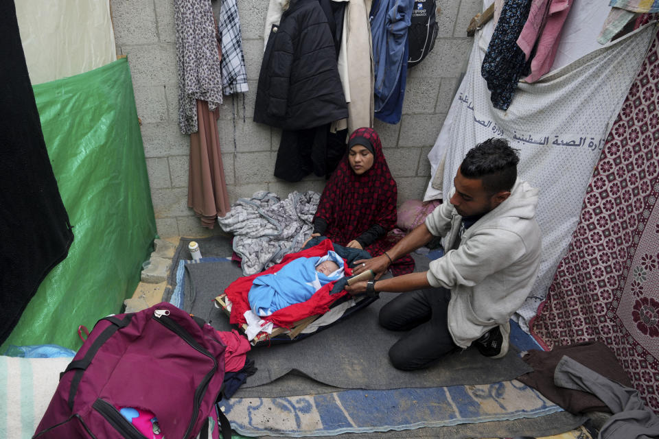 Israa y Salim al-Jamala (derecha), ambos palestinos desplazados por los ataques israelíes en la Franja de Gaza, sentados junto a su recién nacida en un campamento improvisado cerca del Hospital de Al-Aqsa en Deir al Balah, Franja de Gaza, el domingo 10 de diciembre de 2023. (AP Foto/Adel Hana)