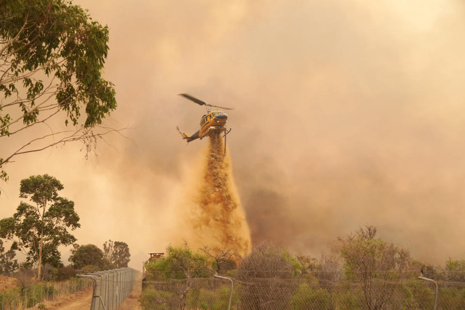 In this photo provided by Department of Fire and Emergency Services, a helicopter drops fire retardant on a fire near Wooroloo, northeast of Perth, Australia, Tuesday, Feb. 2, 2021. An out-of-control wildfire burning northeast of the Australian west coast city of Perth has destroyed dozens of homes and was threatening more. (Evan Collis/DFES via AP)