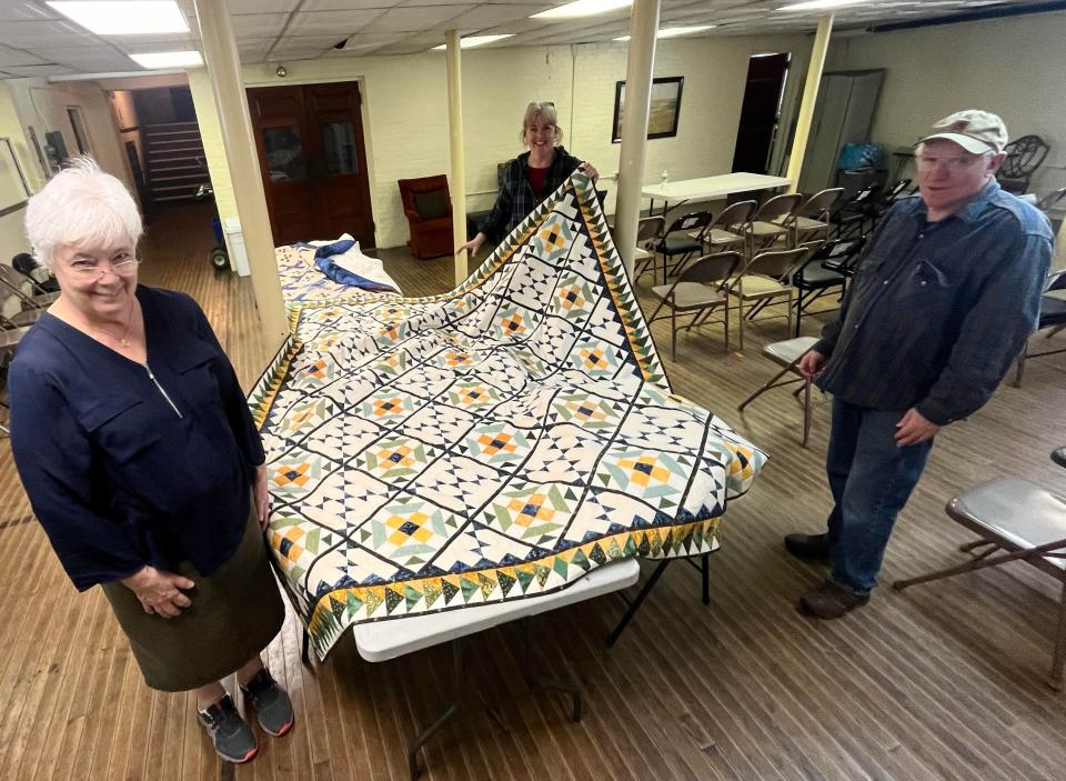 Linda Landis, left, and Maureen Peterson are seen here on Saturday, March 16, 2024, presenting two large, handmade quilts to the director of Taunton's Matthew Mission, Normand Grenier.