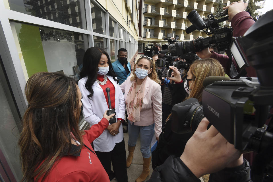 FILE - In this April 19, 2021, file photo Dr. Sylvienash Moma, second left, with hands clasped, declines to speak with the media, outside the Dr. Moma Health & Wellness Clinic at the Satellite Hotel in Colorado Springs, Colo., to address questions that the clinic allegedly improperly stored vaccines, prompting a state investigation. Colorado's health department is recommending that people who received their COVID-19 vaccines at the clinic get revaccinated after a state investigation found the facility improperly stored and handled vaccine doses. The department said Friday, Oct. 8, 2021, it also is permanently banning the clinic from any participation in the federal government's vaccination campaign. (Jerilee Bennett/The Gazette via AP, File)