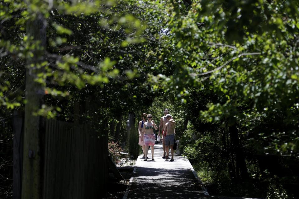 In this June 23, 2013 photo, men and women wander through the streets in the Fire Island community of Cherry Grove, N.Y. Virtually obliterated in a 1938 hurricane, the community now has about 250 houses that can sell for $400,000 or more, and two miles of white, sandy beaches facing the Atlantic accessible via a network of narrow boardwalks. Denizens either walk or get around on golf carts; no cars are permitted in most Fire Island communities. (AP Photo/Seth Wenig)