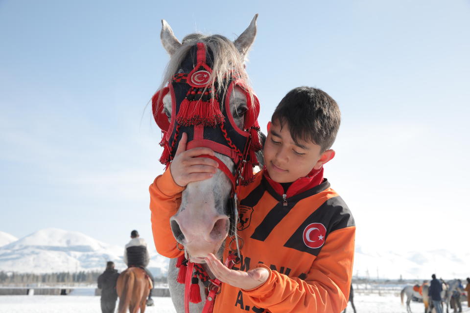 Thirteen-year-old Muhammed Rasit, the youngest member of Uzmanlar, (Experts) sports club, cuddles his horse prior to a game of Cirit, a traditional Turkish equestrian sport that dates back to the martial horsemen who spearheaded the historical conquests of central Asia's Turkic tribes, between the Comrades and the Experts local sporting clubs, in Erzurum, eastern Turkey, Friday, March 5, 2021. The game that was developed more than a 1,000 years ago, revolves around a rider trying to spear his or her opponent with a "javelin" - these days, a rubber-tipped, 100 centimeter (40 inch) length of wood. A rider from each opposing team, which can number up to a dozen players, face each other, alternately acting as the thrower and the rider being chased. Cirit was popular within the Ottoman empire, before it was banned as in the early 19th century. However, its popularity returned as is now one of many traditional sports encouraged by the government and tournaments are often arranged during festivals or to celebrate weddings. (AP Photo/Kenan Asyali)