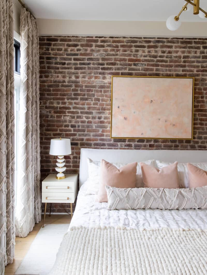 Brick-walled bedroom with white comforter, and white and pink decorative pillows.